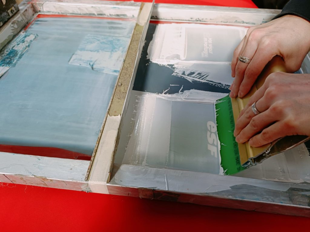 Raclette de la sérigraphe qui applique la peinture blanche sur un logo